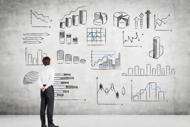A man stands in front of a wall covered in graphs and charts
