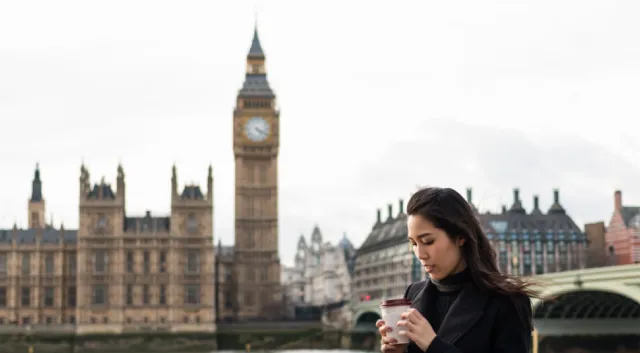 A woman with a takeaway coffee cup with the Houses of Parliament in the background