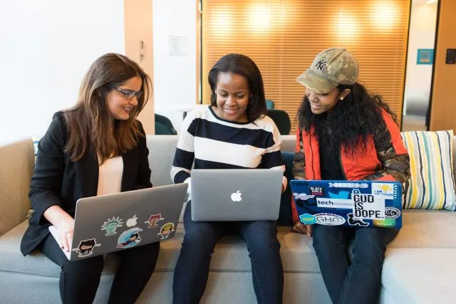 Three women talk with laptops on their knees