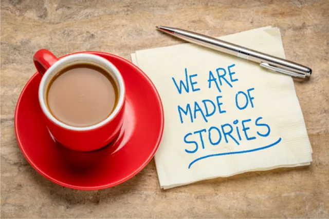 A cup of tea in a red cup and saucer sits next to a piece of paper saying 'we are made of stories'