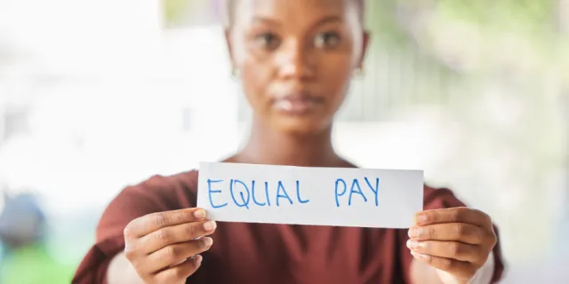 Woman holding a piece of paper reading 'Equal Pay'